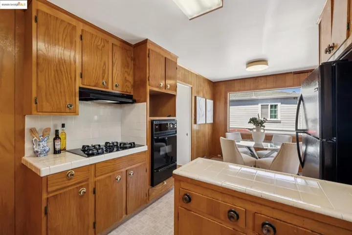 Kitchen featuring black appliances, brown cabinetry, tasteful backsplash, a warming drawer, and tile countertops