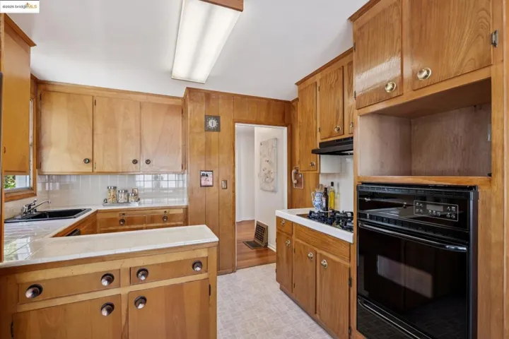 Kitchen featuring black appliances, tasteful backsplash, brown cabinets, a warming drawer, and under cabinet range hood