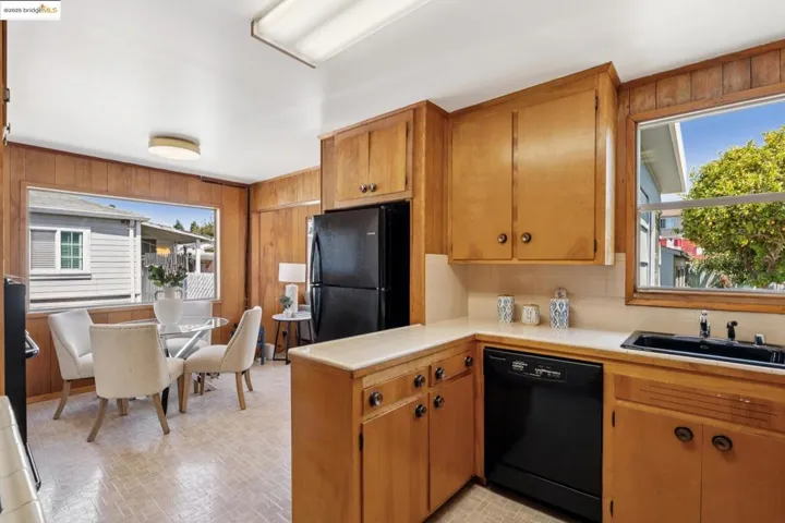 Kitchen with wood walls, black appliances, brown cabinetry, tile counters, and brick patterned flooring