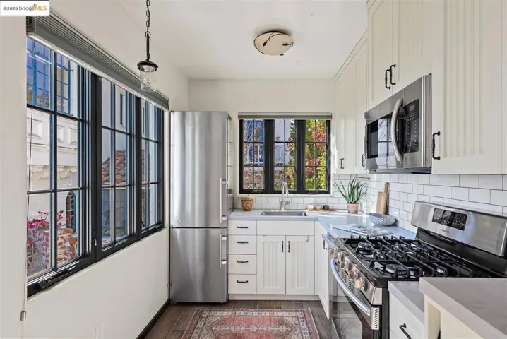 Kitchen with appliances with stainless steel finishes, backsplash, decorative light fixtures, dark wood-style flooring, and white cabinetry