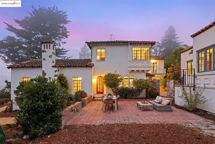 Back of property at dusk with a balcony, a patio, a chimney, a tile roof, and stucco siding