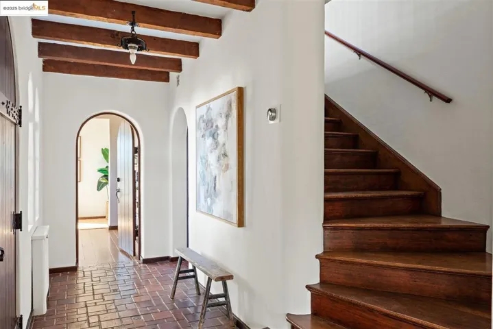 Stairway featuring brick flooring, beam ceiling, and arched walkways
