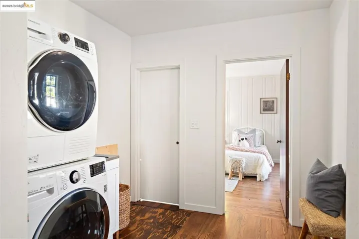 Laundry area with dark wood finished floors and stacked washing machine and dryer
