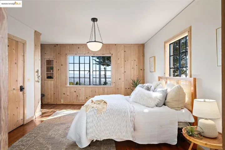 Bedroom with wood walls, multiple windows, and wood finished floors