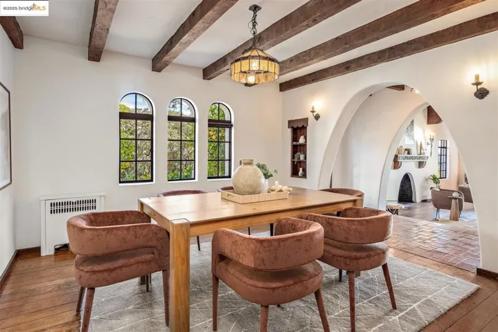 Dining room featuring arched walkways, wood-type flooring, radiator heating unit, and beam ceiling
