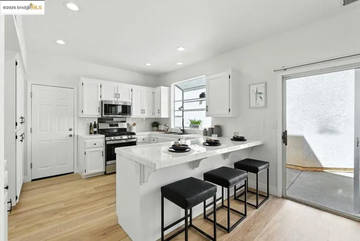 Kitchen featuring backsplash, white cabinets, tile countertops, a kitchen breakfast bar, and appliances with stainless steel finishes
