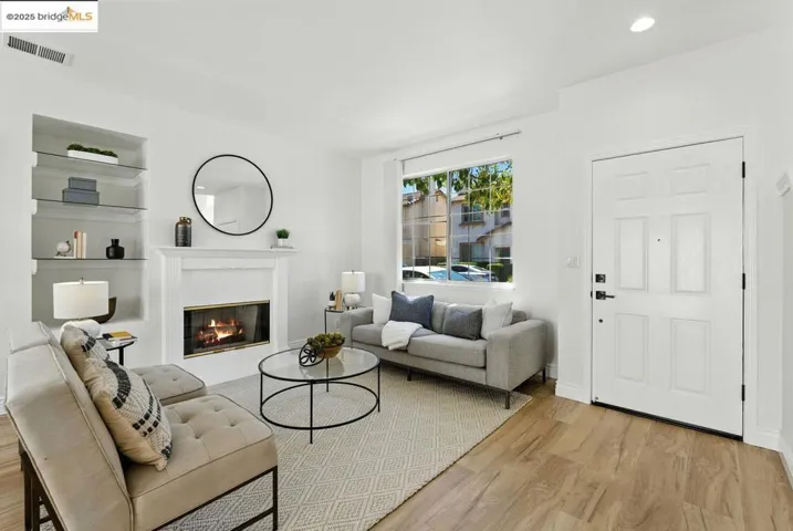 Living area with wood finished floors, built in features, a glass covered fireplace, and recessed lighting