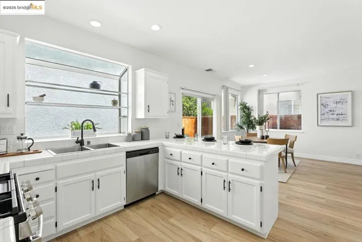 Kitchen featuring a peninsula, white cabinetry, stainless steel appliances, tile counters, and recessed lighting