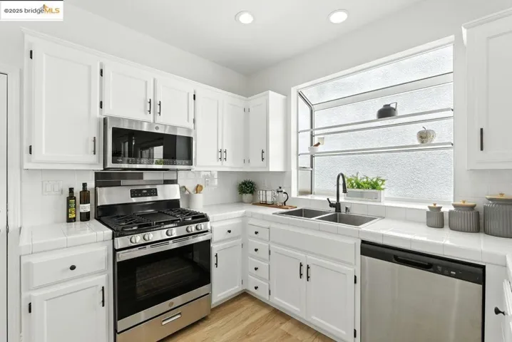 Kitchen with tile countertops, stainless steel appliances, white cabinets, and recessed lighting
