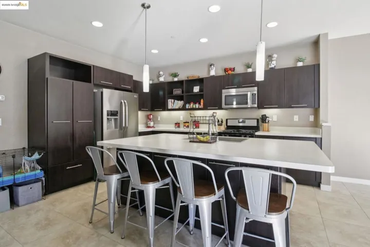 Kitchen with dark brown cabinets, open shelves, a breakfast bar area, an island with sink, and light countertops
