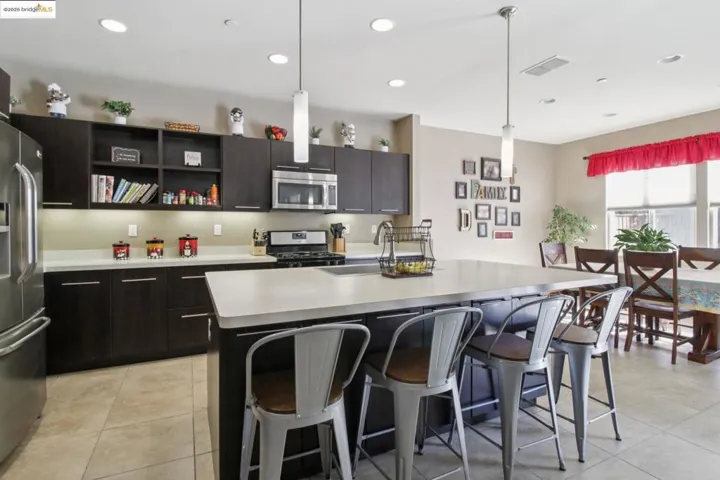 Kitchen with pendant lighting, appliances with stainless steel finishes, a kitchen breakfast bar, light countertops, and light tile patterned floors