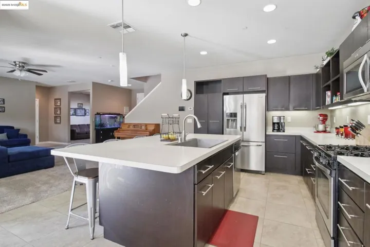 Kitchen with open shelves, appliances with stainless steel finishes, open floor plan, light countertops, and a kitchen breakfast bar
