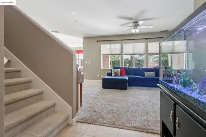 Living area featuring light tile patterned floors, light carpet, stairway, and ceiling fan