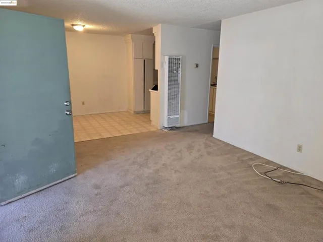 Empty room featuring a textured ceiling, a heating unit, and light carpet