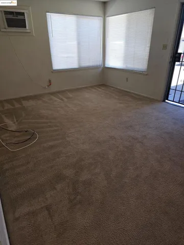 Carpeted spare room with baseboards and an AC wall unit