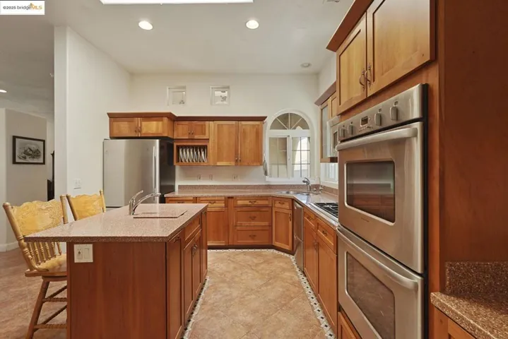 Kitchen featuring stainless steel appliances, recessed lighting, a breakfast bar, brown cabinetry, and an island with sink