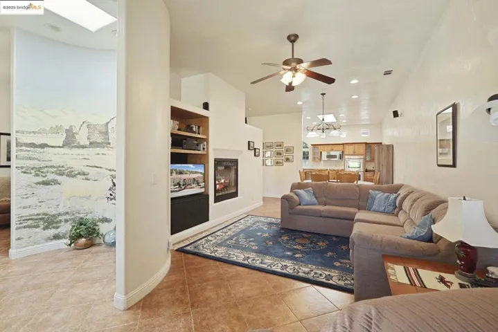 Living area with light tile patterned flooring, built in features, a multi sided fireplace, a chandelier, and a ceiling fan