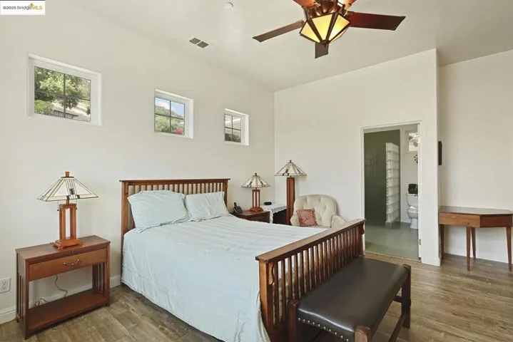 Bedroom with wood finished floors, a ceiling fan, and ensuite bath