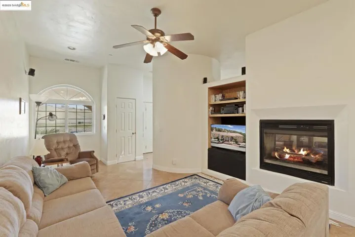 Living area featuring a multi sided fireplace, a ceiling fan, light tile patterned floors, and built in features