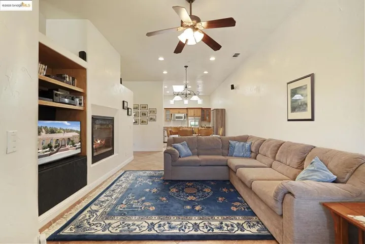Living room with a glass covered fireplace, light tile patterned flooring, a chandelier, a high ceiling, and a ceiling fan