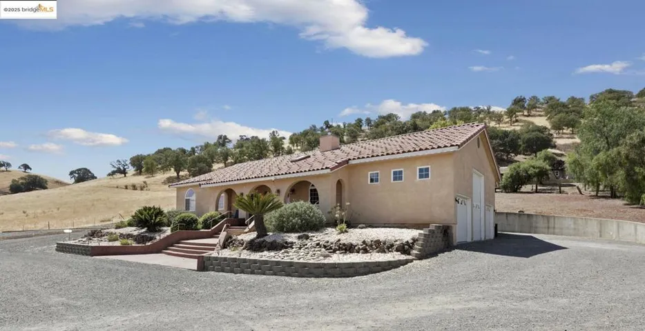 Mediterranean / spanish-style home with gravel driveway, stucco siding, a chimney, a tiled roof, and a garage