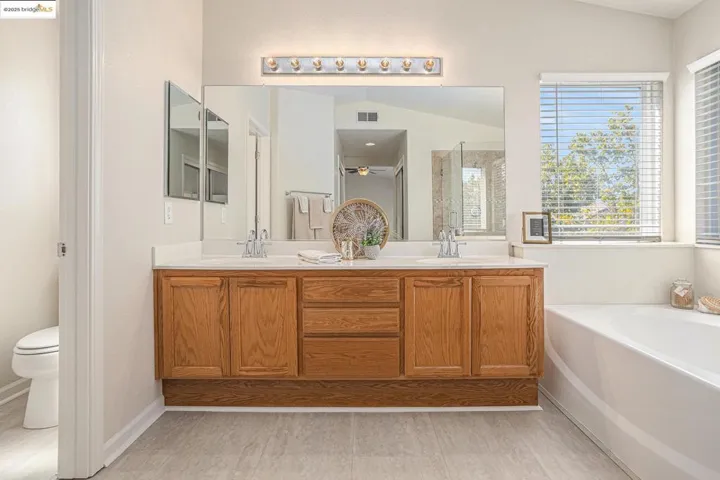 Full bathroom with a stall shower, double vanity, a garden tub, light wood-type flooring, and vaulted ceiling