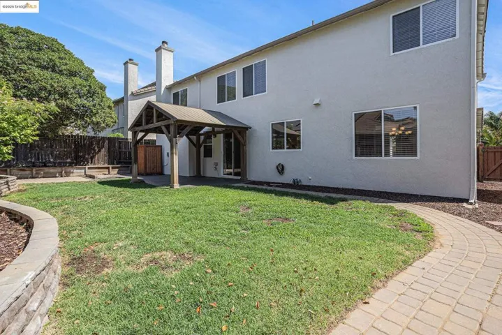 Back of house featuring paver walkway, stucco siding, a patio area, a fenced backyard, and a gazebo
