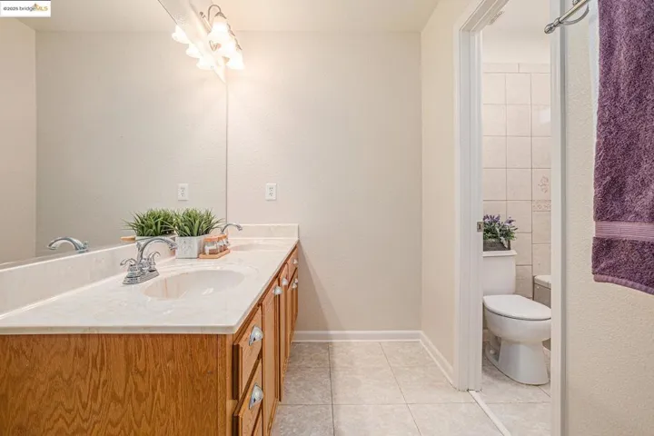 Full bath featuring double vanity, light vinyl tile patterned floors, with toilet room.