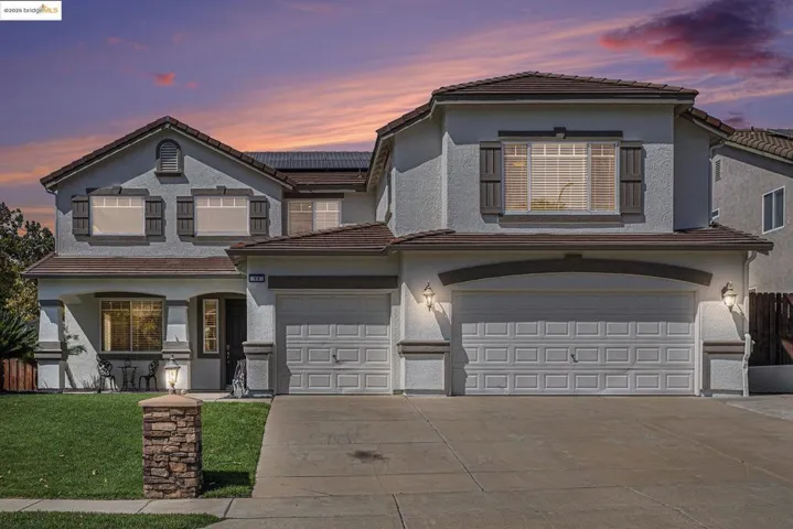View of front facade with a tile roof, solar panels, concrete driveway, and stucco siding