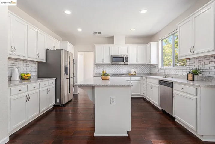 Kitchen with white cabinetry, stainless steel appliances, a kitchen island, light stone countertops, and a kitchen breakfast bar