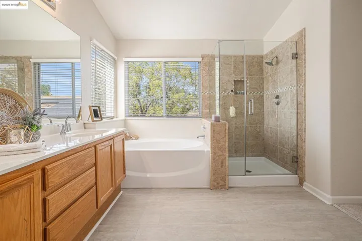 Bathroom with a garden bathtub, shower stall with seamless glass enclosure, double vanity, and light vinyl tile patterned floors.