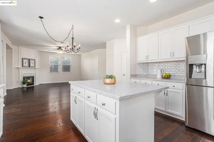 Kitchen with white cabinetry, stainless steel refrigerator with ice dispenser, a center island, tasteful backsplash, and hanging light fixtures