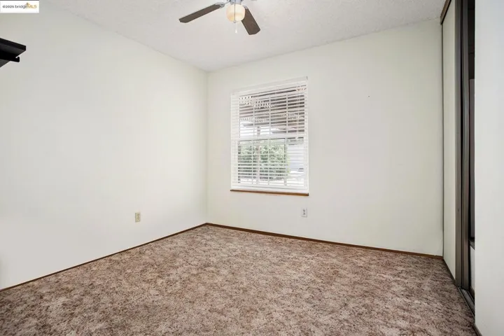 Carpeted empty room with a textured ceiling and ceiling fan