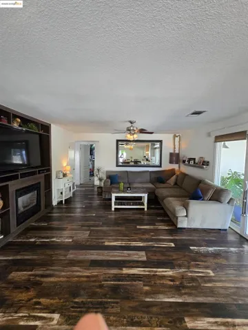 Living area featuring a textured ceiling, dark wood-type flooring, and a ceiling fan