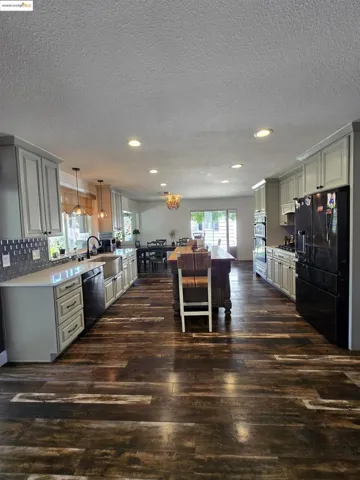 Kitchen featuring decorative light fixtures, black fridge, dark wood-style floors, a textured ceiling, and tasteful backsplash