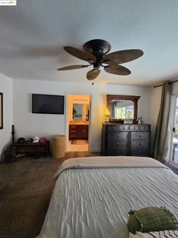 Bedroom with a textured ceiling, carpet, a ceiling fan, and connected bathroom