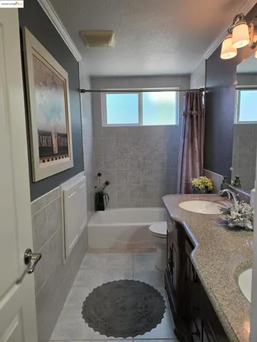 Bathroom featuring shower / tub combo, double vanity, a textured ceiling, light tile patterned floors, and tile walls