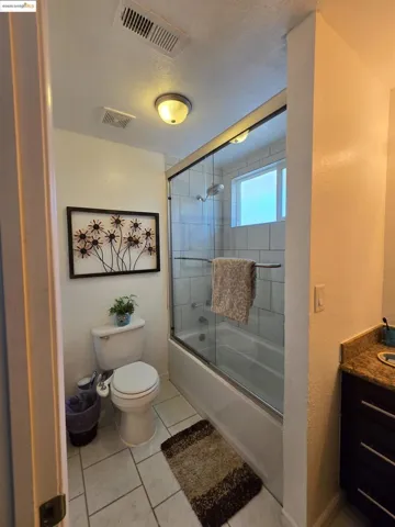Full bath featuring bath / shower combo with glass door, vanity, light tile patterned floors, a textured ceiling, and a textured wall