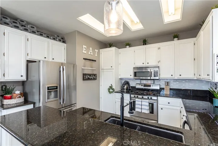 Modern kitchen with white cabinets, stainless appliances, granite counters and new tile backsplash.