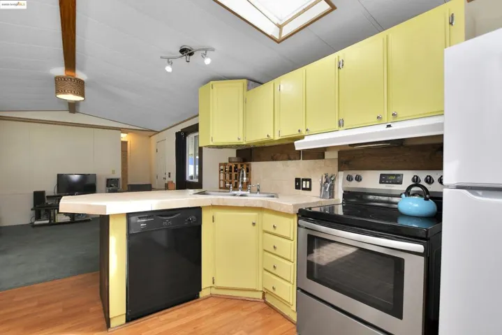 Kitchen featuring stainless steel range with electric stovetop, a peninsula, freestanding refrigerator, dishwasher, and lofted ceiling