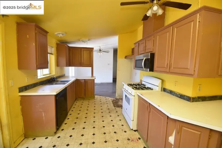 Kitchen with white range with gas cooktop, a ceiling fan, light flooring, stainless steel microwave, and light countertops
