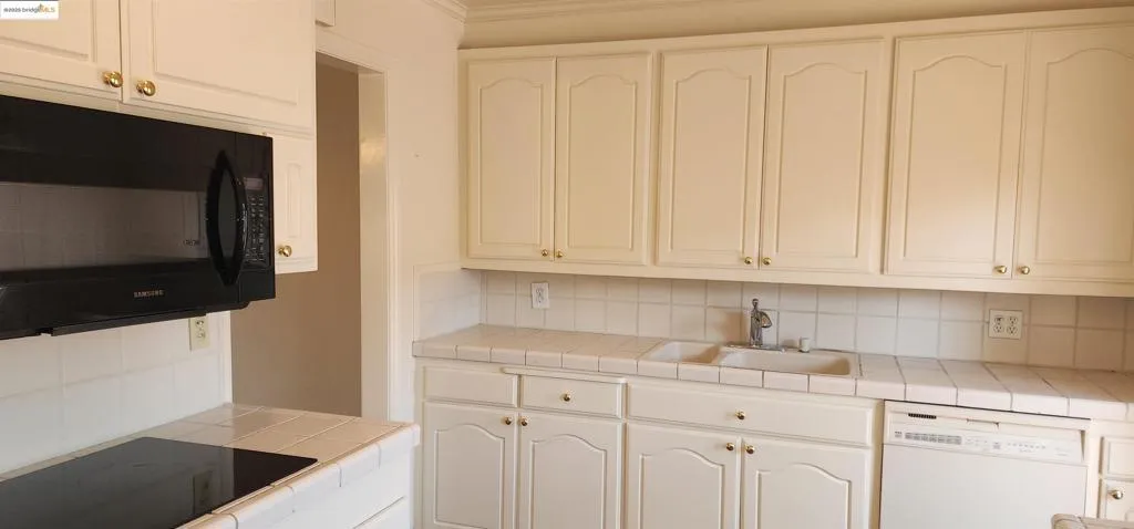 Kitchen featuring backsplash, tile counters, black appliances, and white cabinetry
