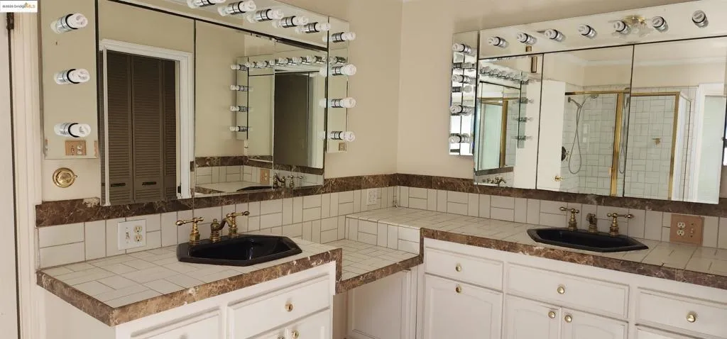 Bathroom with a stall shower, water heater, two vanities, and backsplash