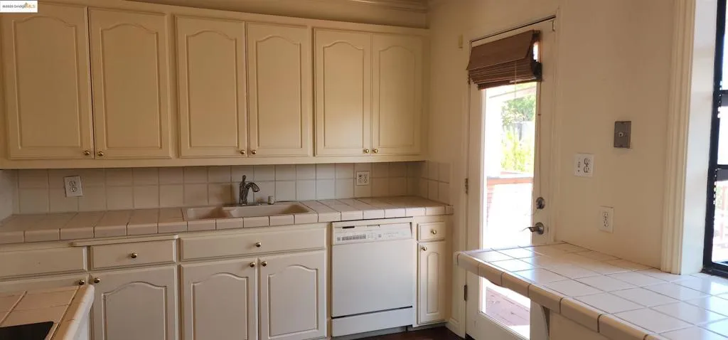 Kitchen featuring tile countertops, dishwasher, tasteful backsplash, and white cabinets