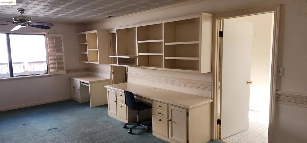 Unfurnished office with built in desk, ceiling fan, carpet, and crown molding