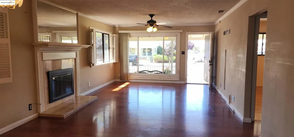 Unfurnished living room with ornamental molding, a textured ceiling, dark wood-type flooring, a tiled fireplace, and a ceiling fan