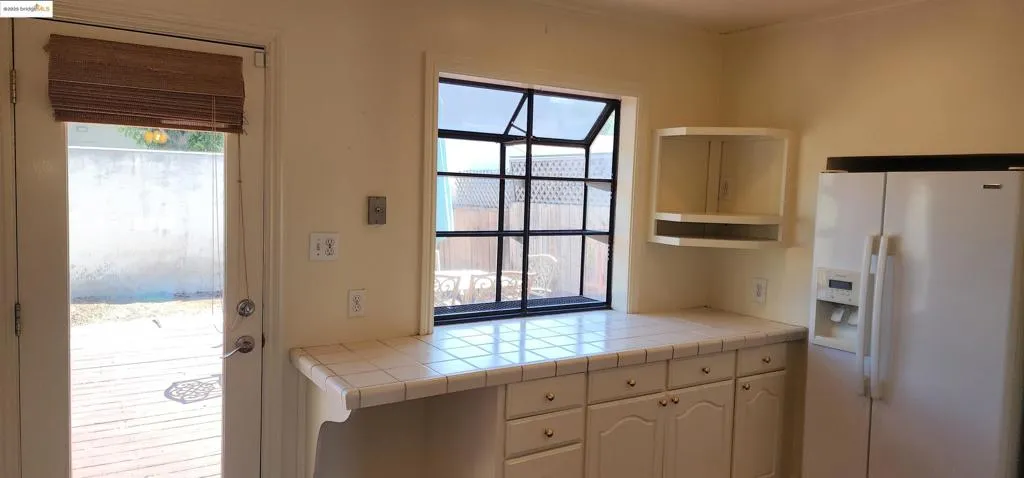 Kitchen featuring white refrigerator with ice dispenser, tile counters, and white cabinetry