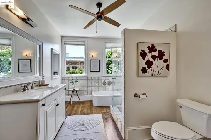 Bathroom with tile walls, a freestanding bath, vanity, dark wood-style flooring, and ceiling fan