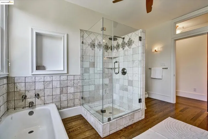 Full bath featuring dark wood-type flooring, a stall shower, a garden tub, and ceiling fan