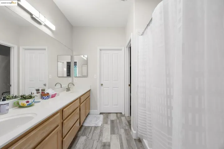 Bathroom with double vanity, light wood finished floors, and curtained shower